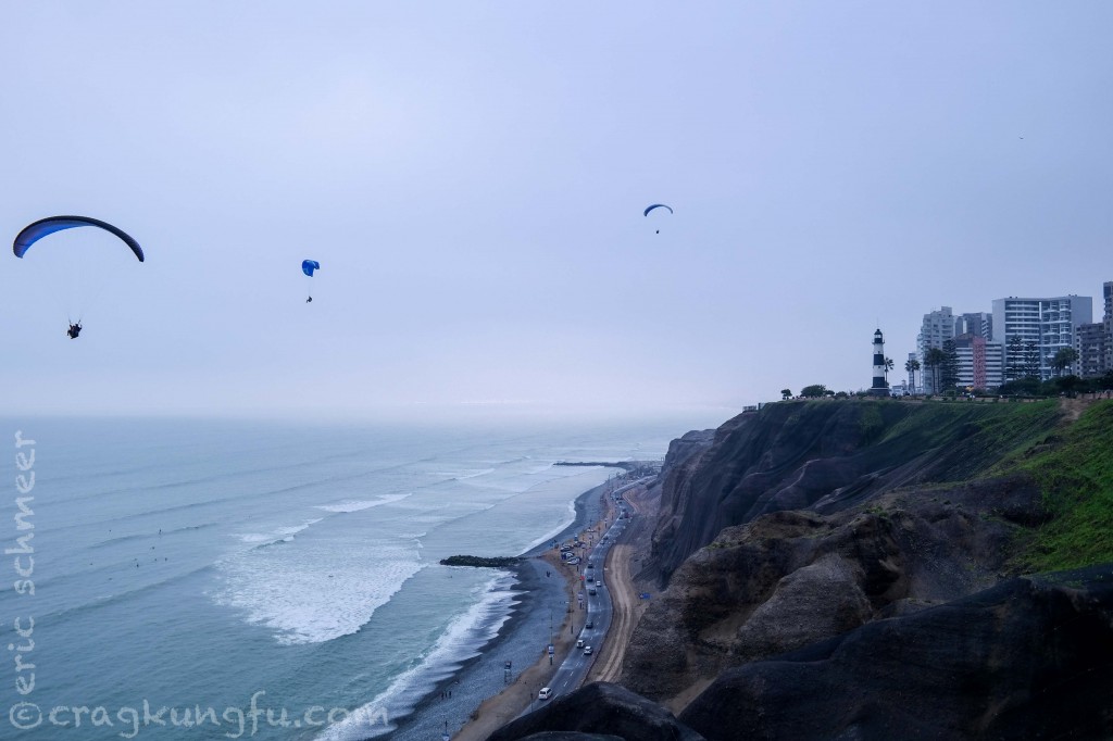 Paragliders and surfers play by the cliffs on the malecon